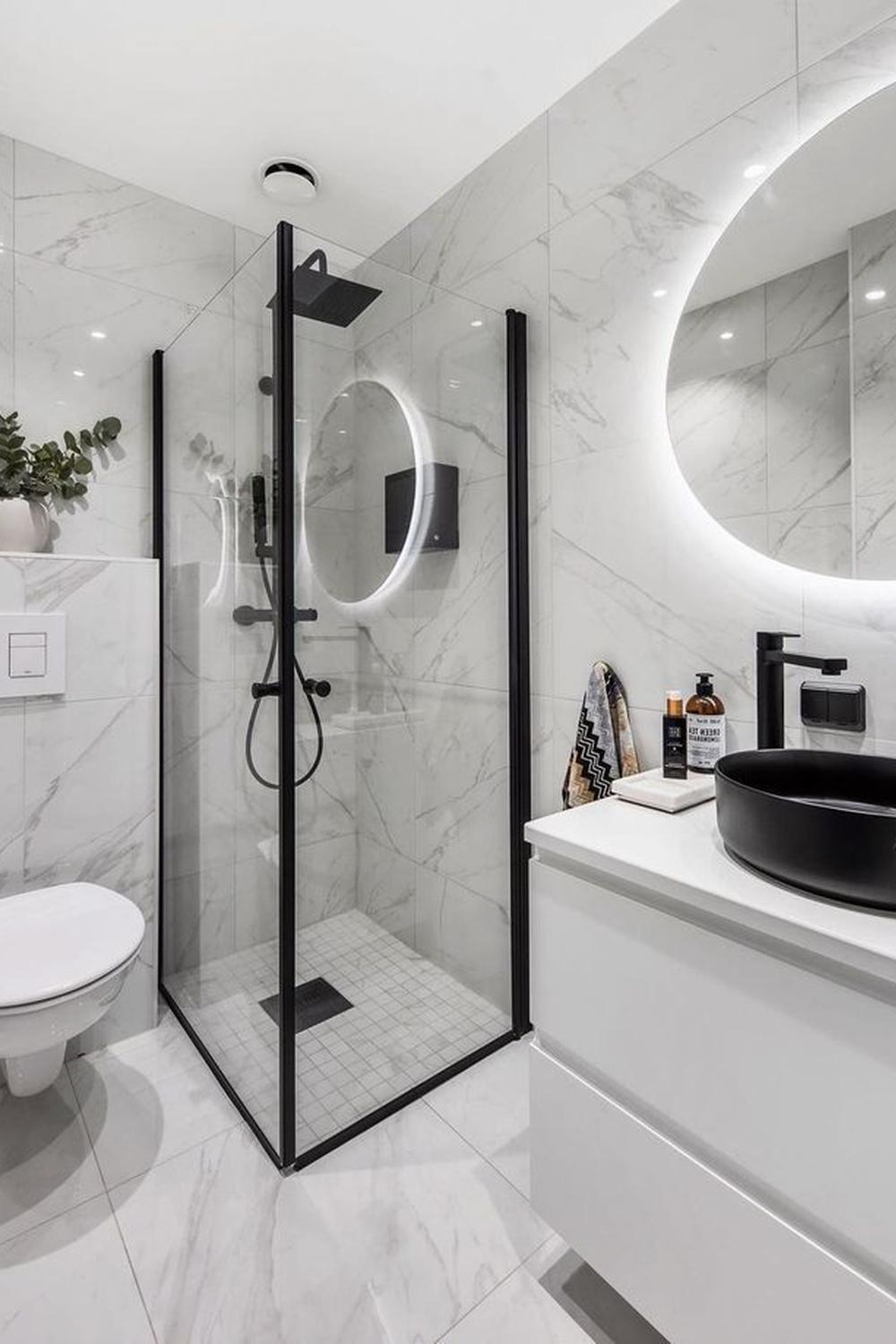 Modern bathroom showcasing white marble tiles, a glass shower enclosure, and a black rainfall showerhead for a contemporary aesthetic.
