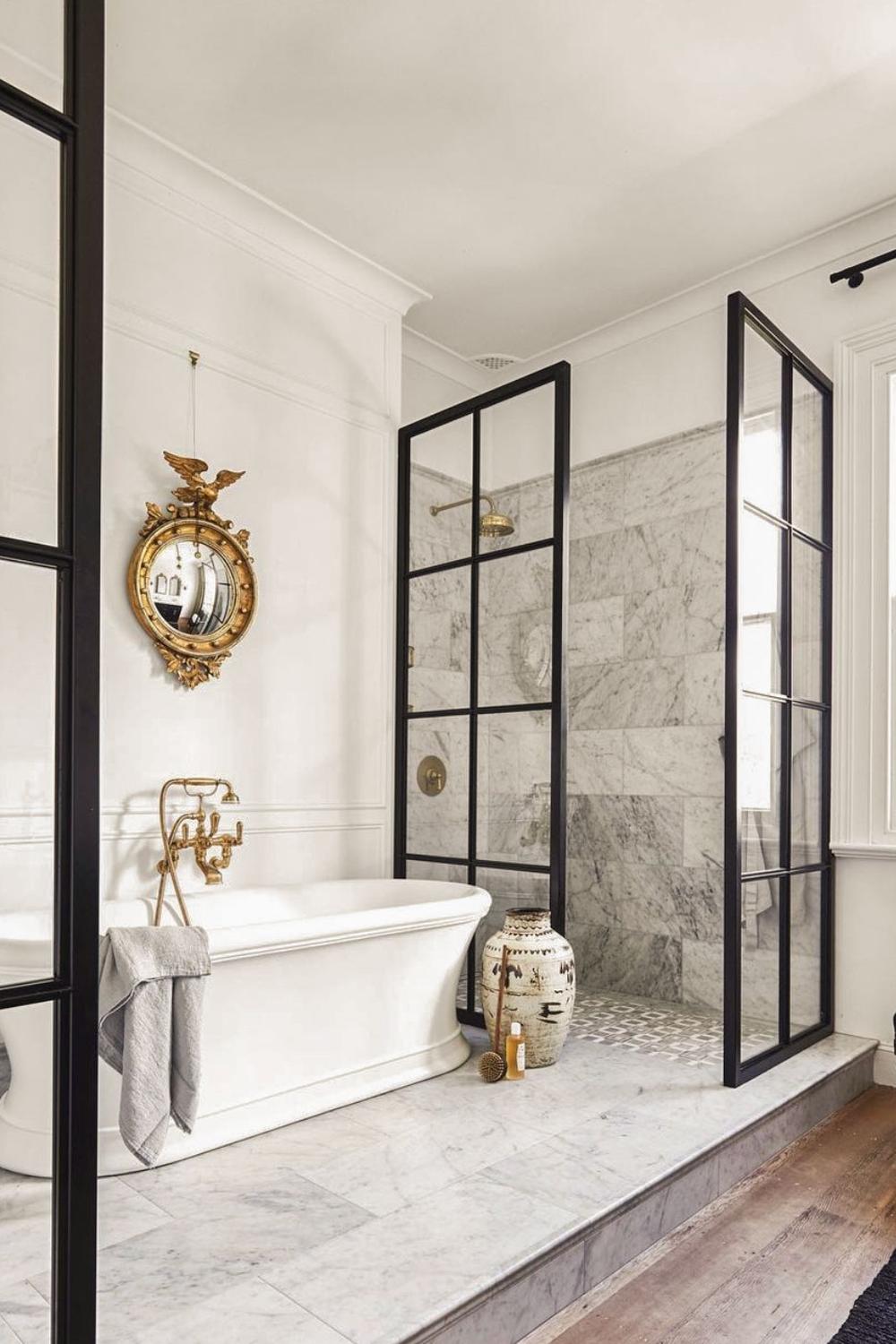 A luxurious bathroom featuring a white freestanding bath, a black-framed glass shower enclosure, and an elegant vintage-style bathtub faucet.