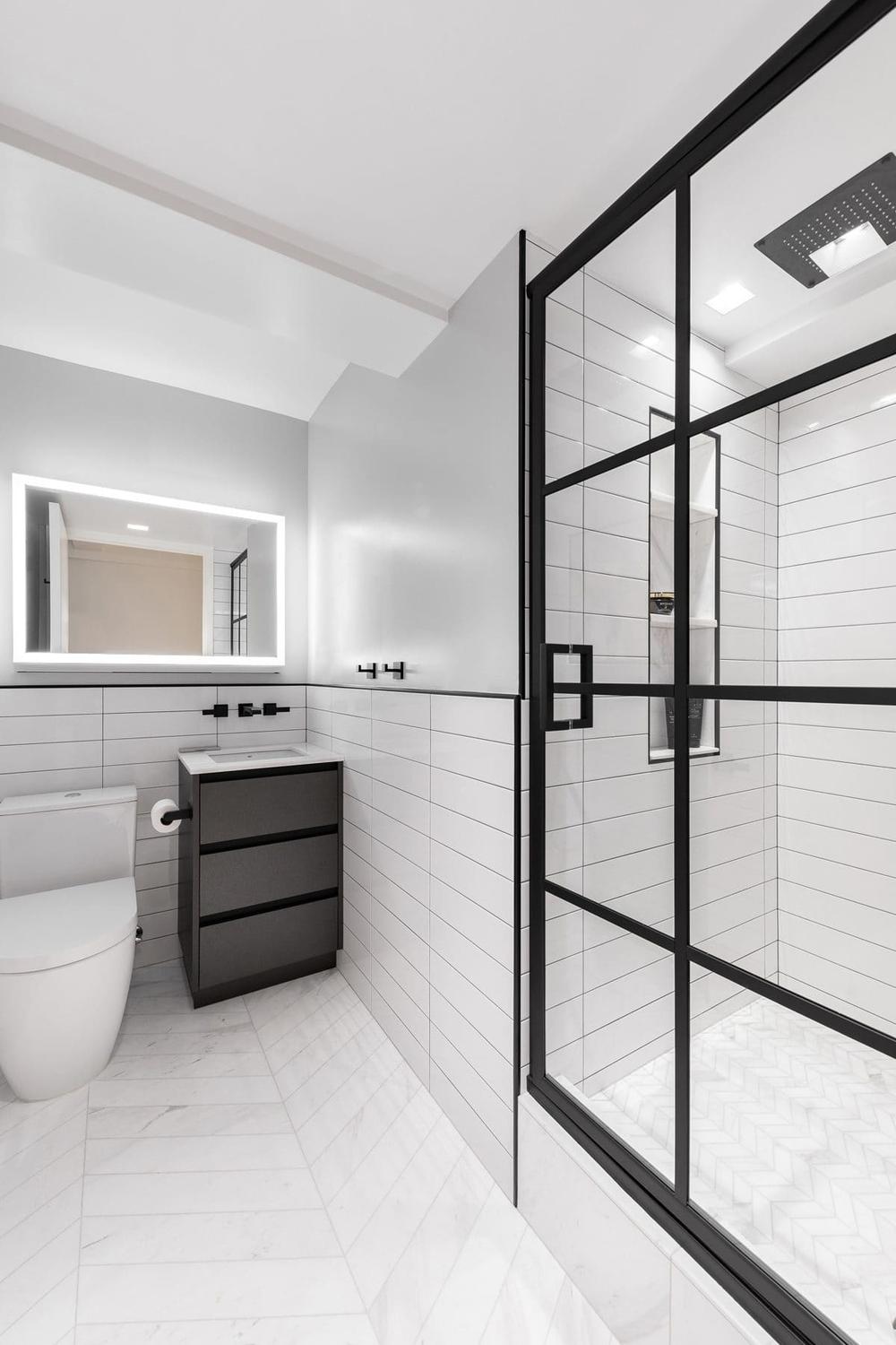 An airy, light-infused bathroom with subtle elegance portrayed through sleek fixtures, rounded mirror, and black accents enhancing the spacious look.