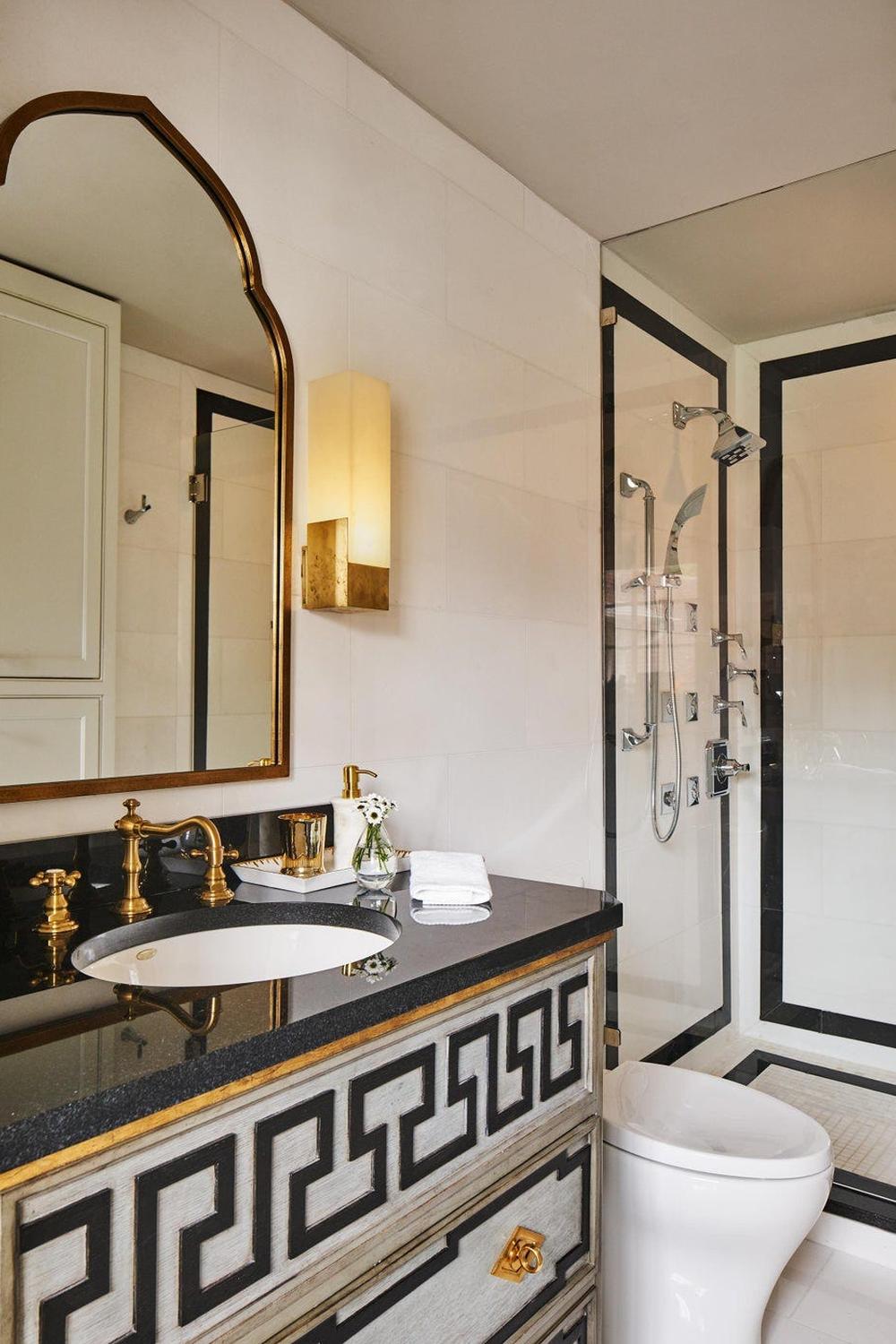 A lavish bathroom with intricate cabinetry, dark granite countertops, and a beautifully arched mirror that reflects light effectively for an elegant design.