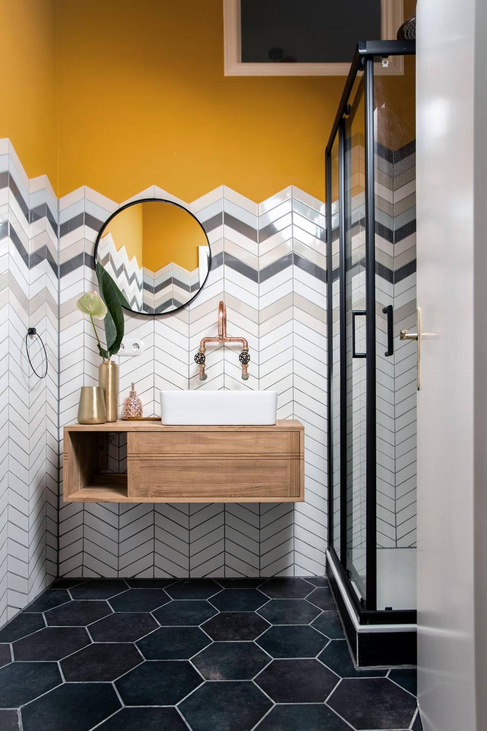 Baño moderno con pared de acento amarilla y azulejos chevron en blanco y gris.