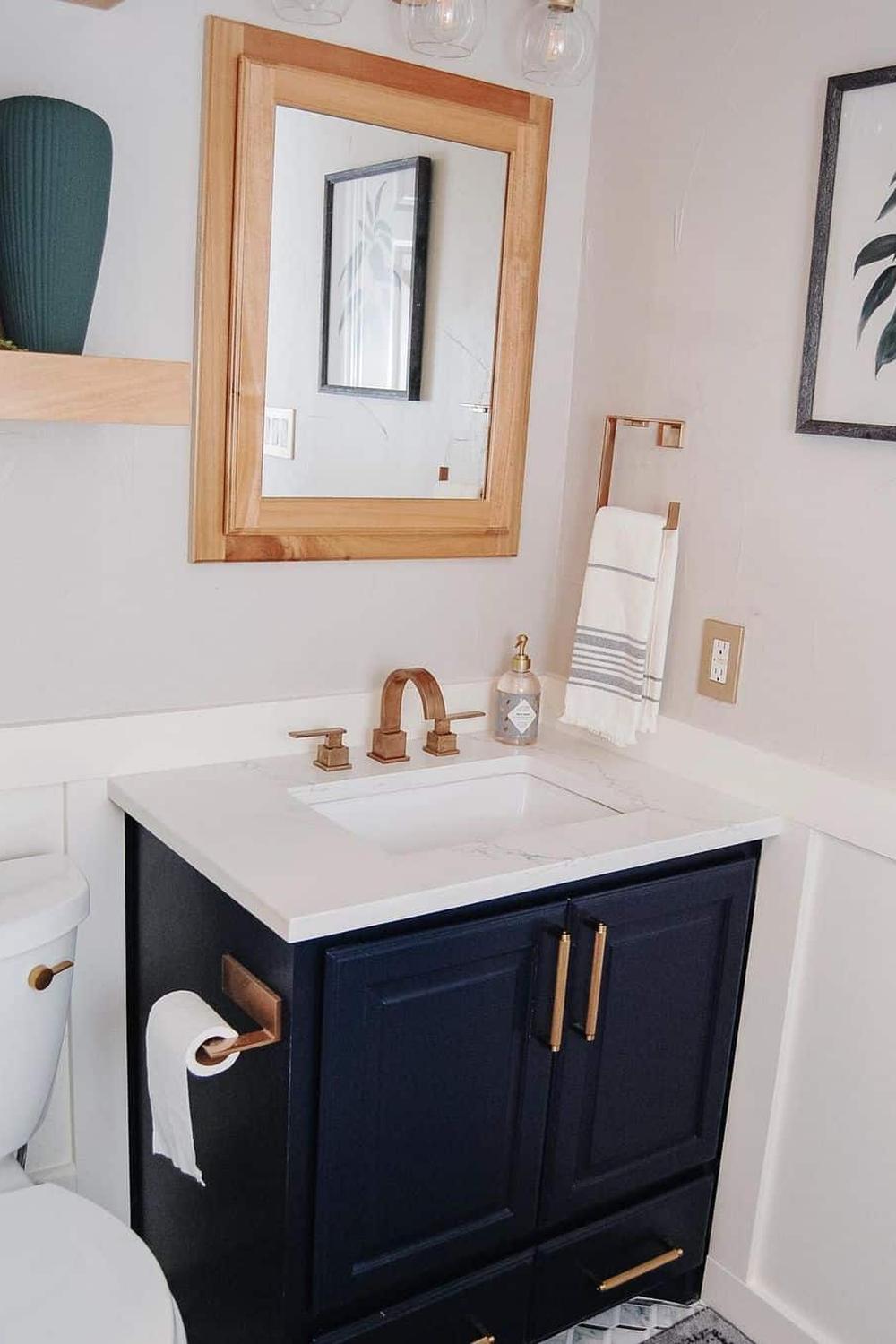 A modern American farmhouse bathroom featuring navy blue black cabinets with gold handles, white countertops, and a stylish vanity.