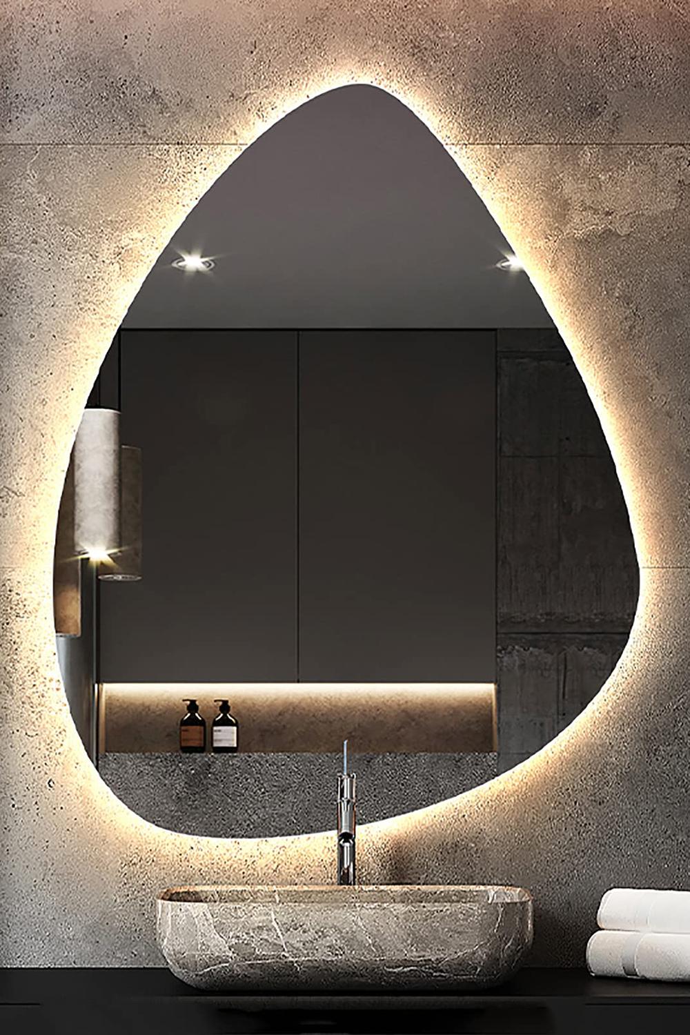 Teardrop-shaped backlit mirror against raw concrete wall in a modern bathroom setting