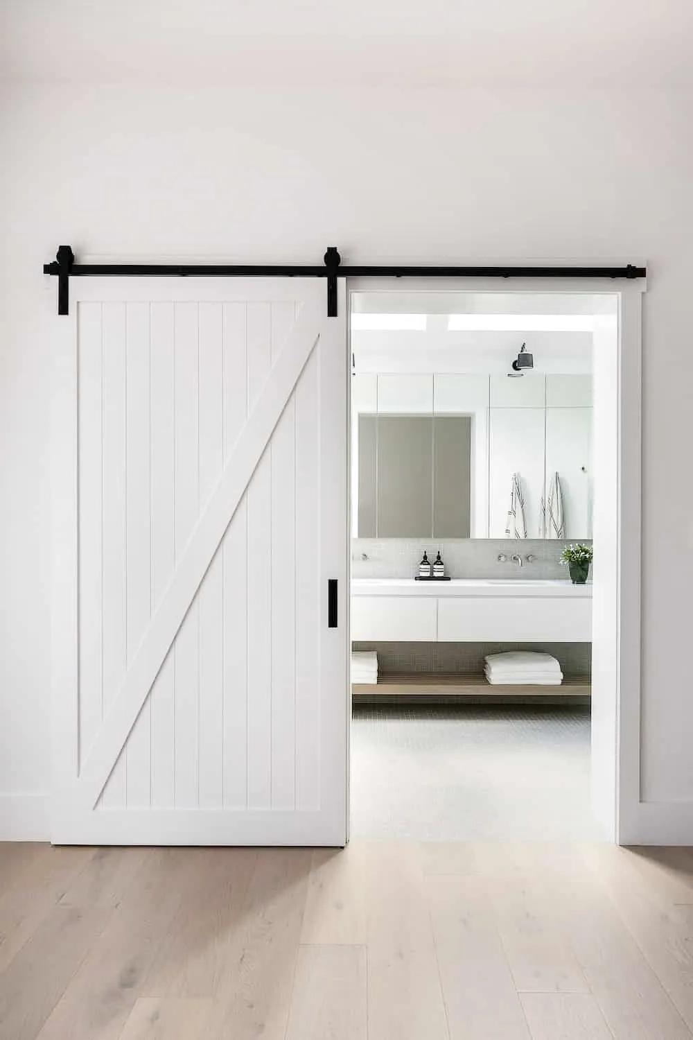 Entrada moderna a un baño con puerta de granero blanca y vanidad clara