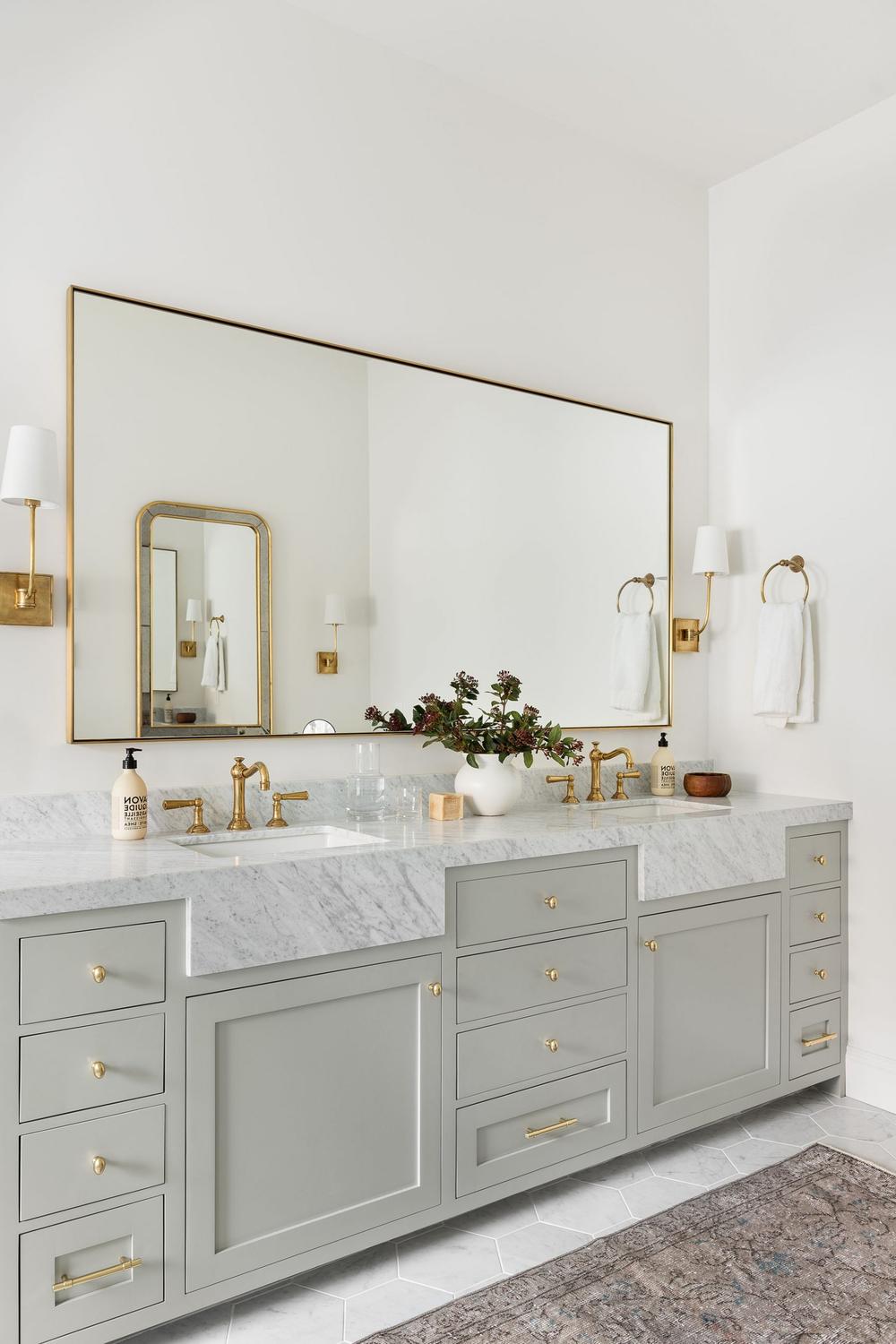 Bathroom with dark and light contrasting elements featuring a stylish mirror and sconces.