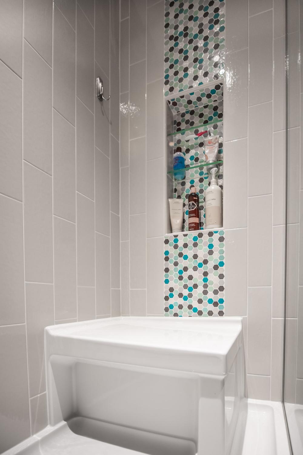 A modern shower space showcasing glossy light gray tiles and a vivid mosaic.