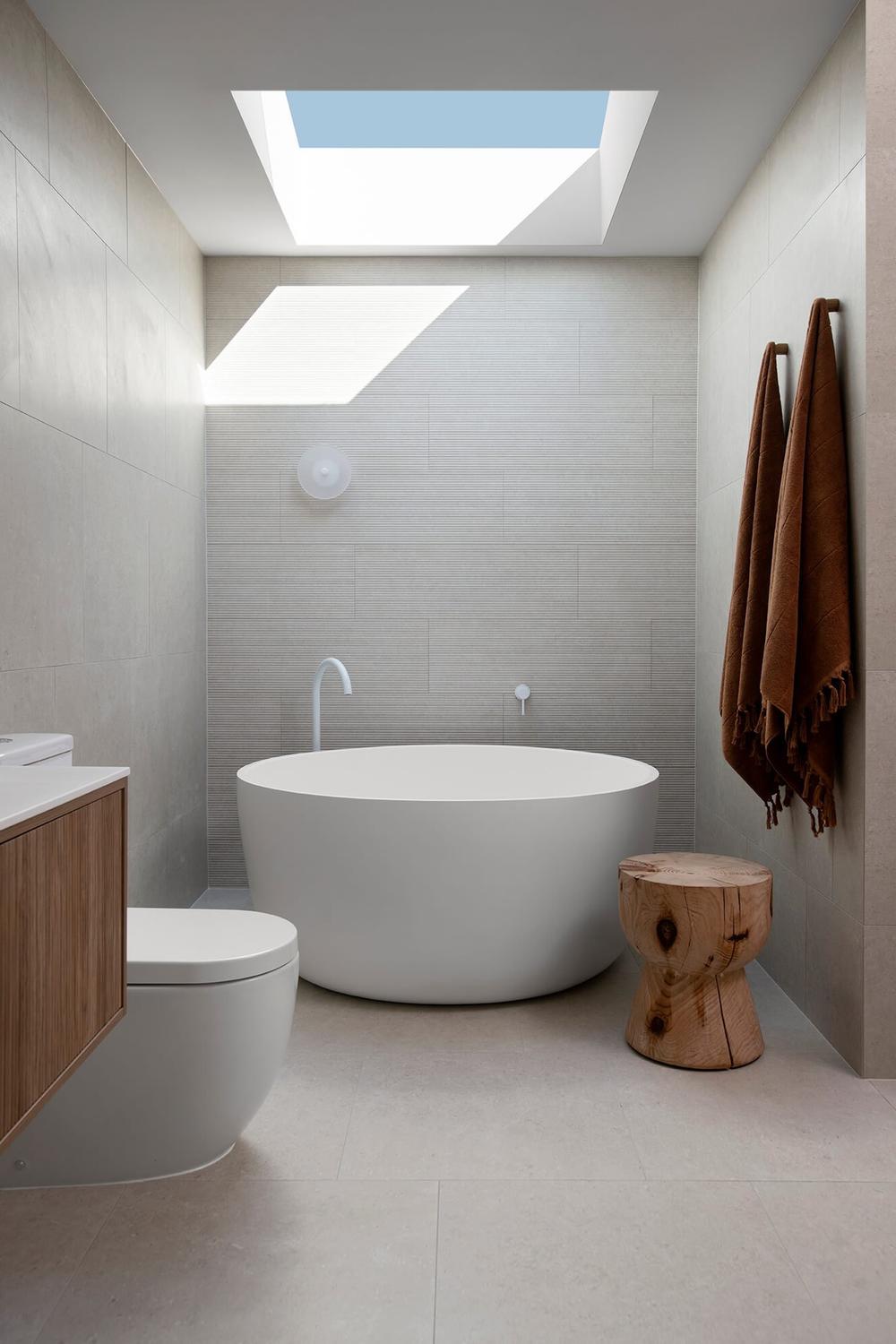 A modern bathroom showcasing soft beige and light gray tiles, a freestanding white tub, and wooden cabinetry for a calming atmosphere.