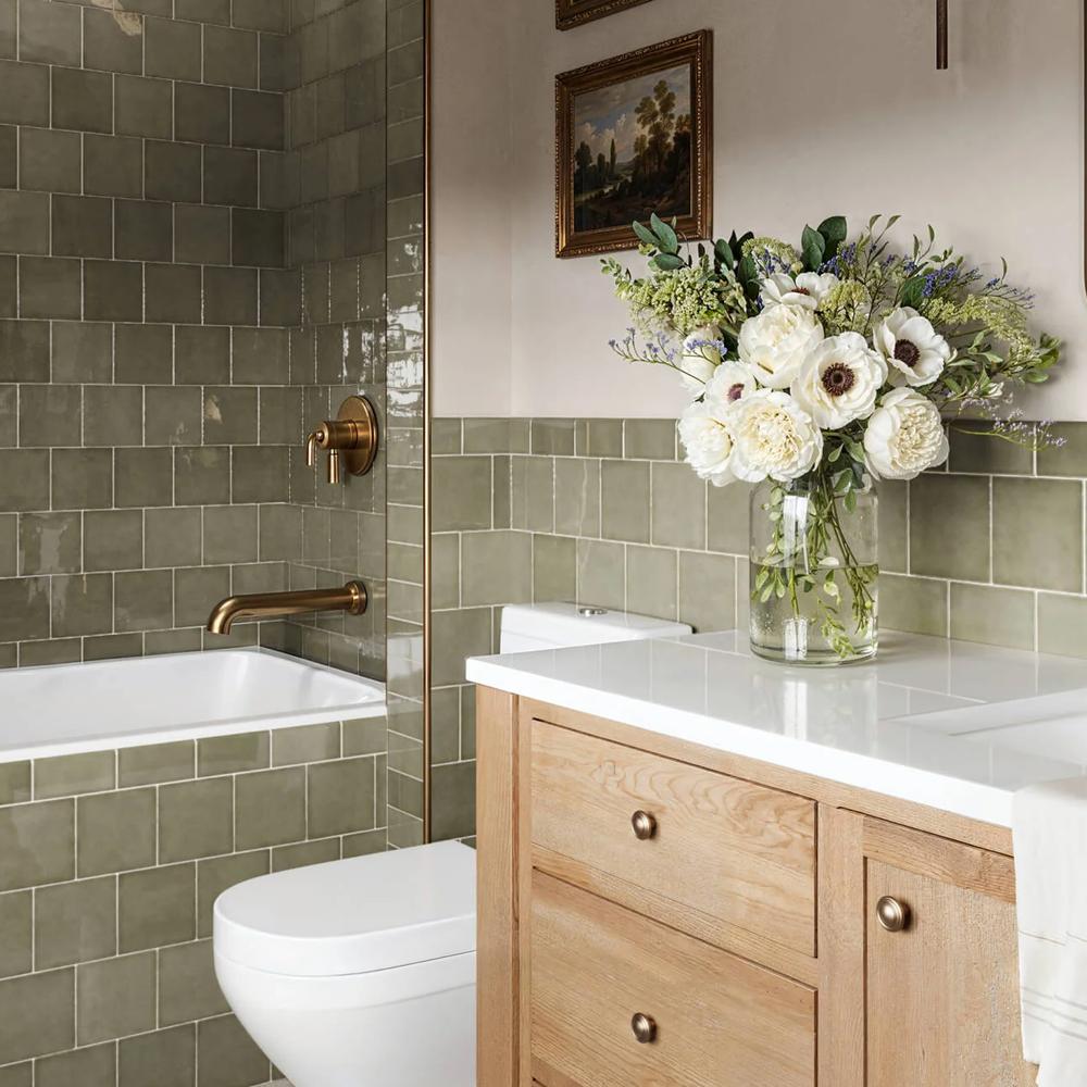 A modern bathroom featuring glossy olive-green subway tiles, brass fixtures, and a wooden vanity creating a natural atmosphere.