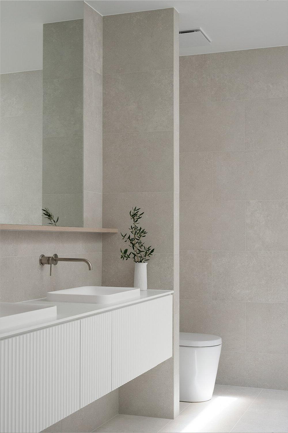 A minimalist bathroom designed with light gray and beige tiles, featuring a dual vanity, ambient lighting, and a potted plant for a fresh touch.