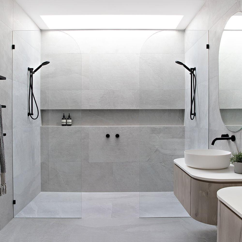 A minimalist gray bathroom with transparent glass shower walls showcasing sleek black fixtures and organic shapes.