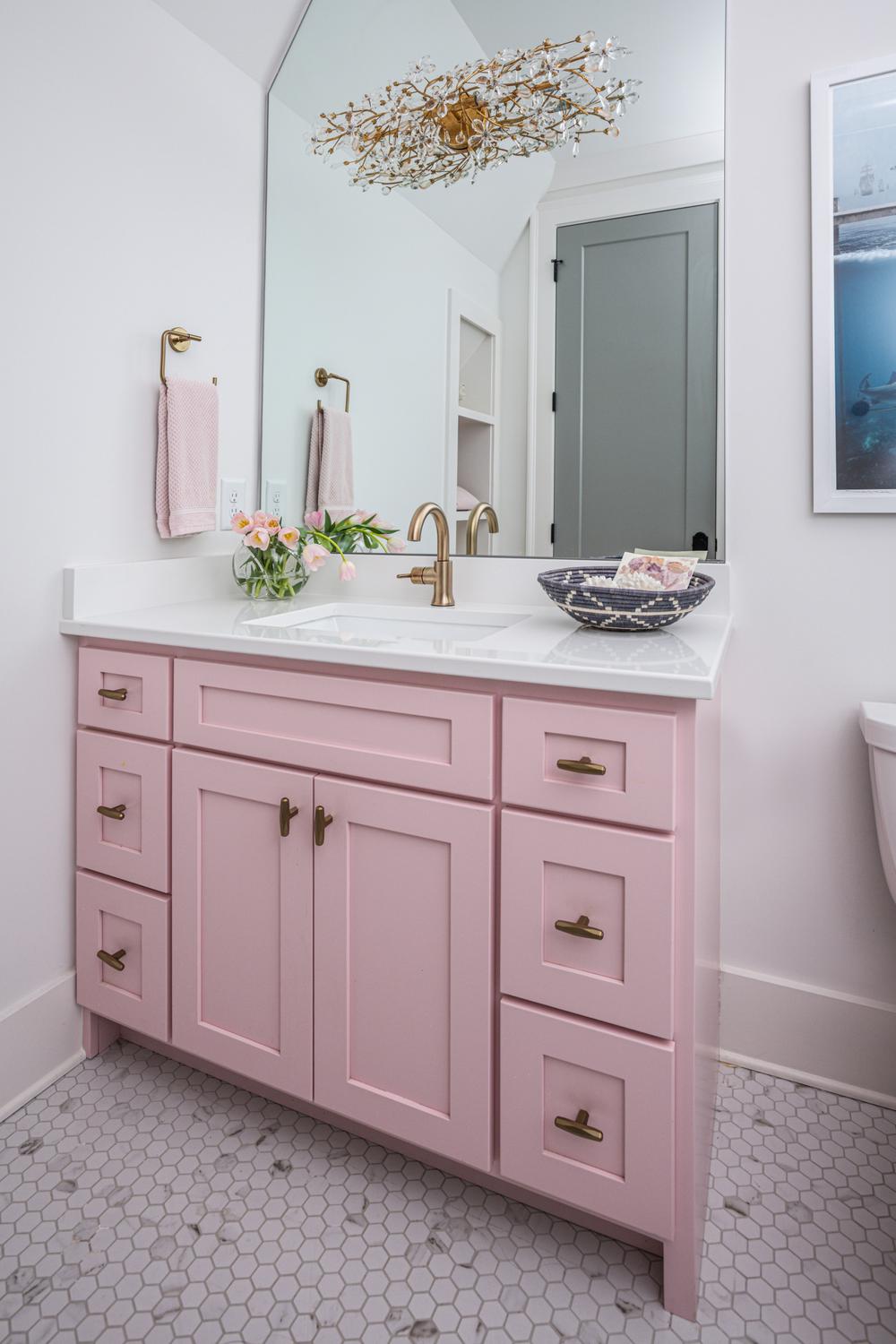 Pastel pink bathroom vanity featuring elegant brass fixtures and natural decorative elements.