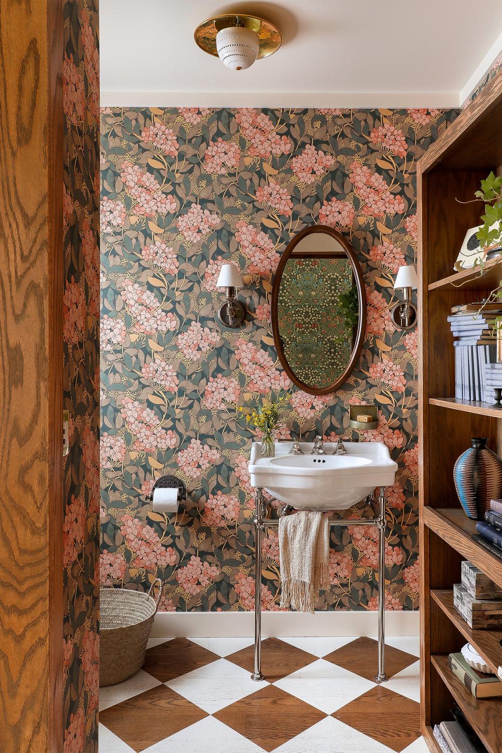 A beautifully styled bathroom featuring vintage floral wallpaper with pink blossoms on a dark green background.