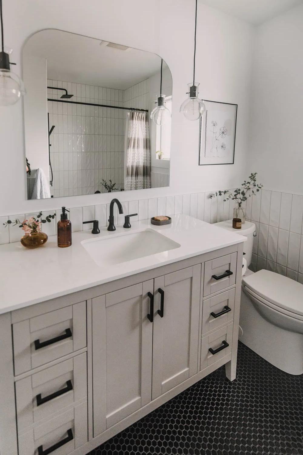 A modern bathroom with light gray vanity, black fixtures, and stylish pendant lights.