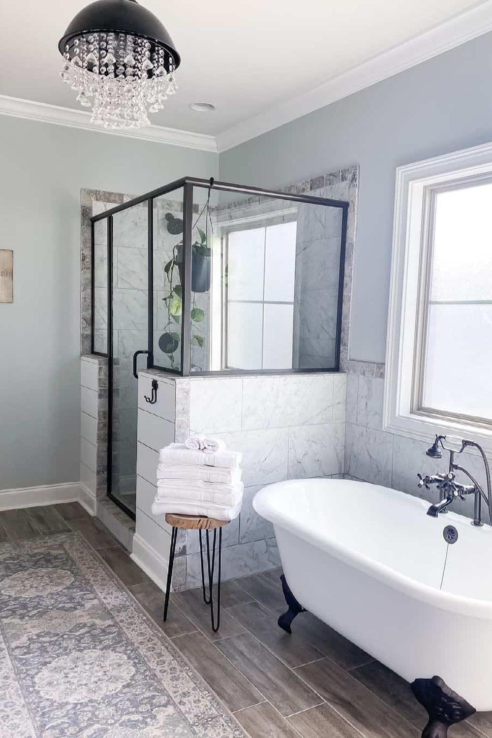 Elegant bathroom design with a white clawfoot tub next to a glass shower enclosure, soft blue walls, and wooden-like flooring.
