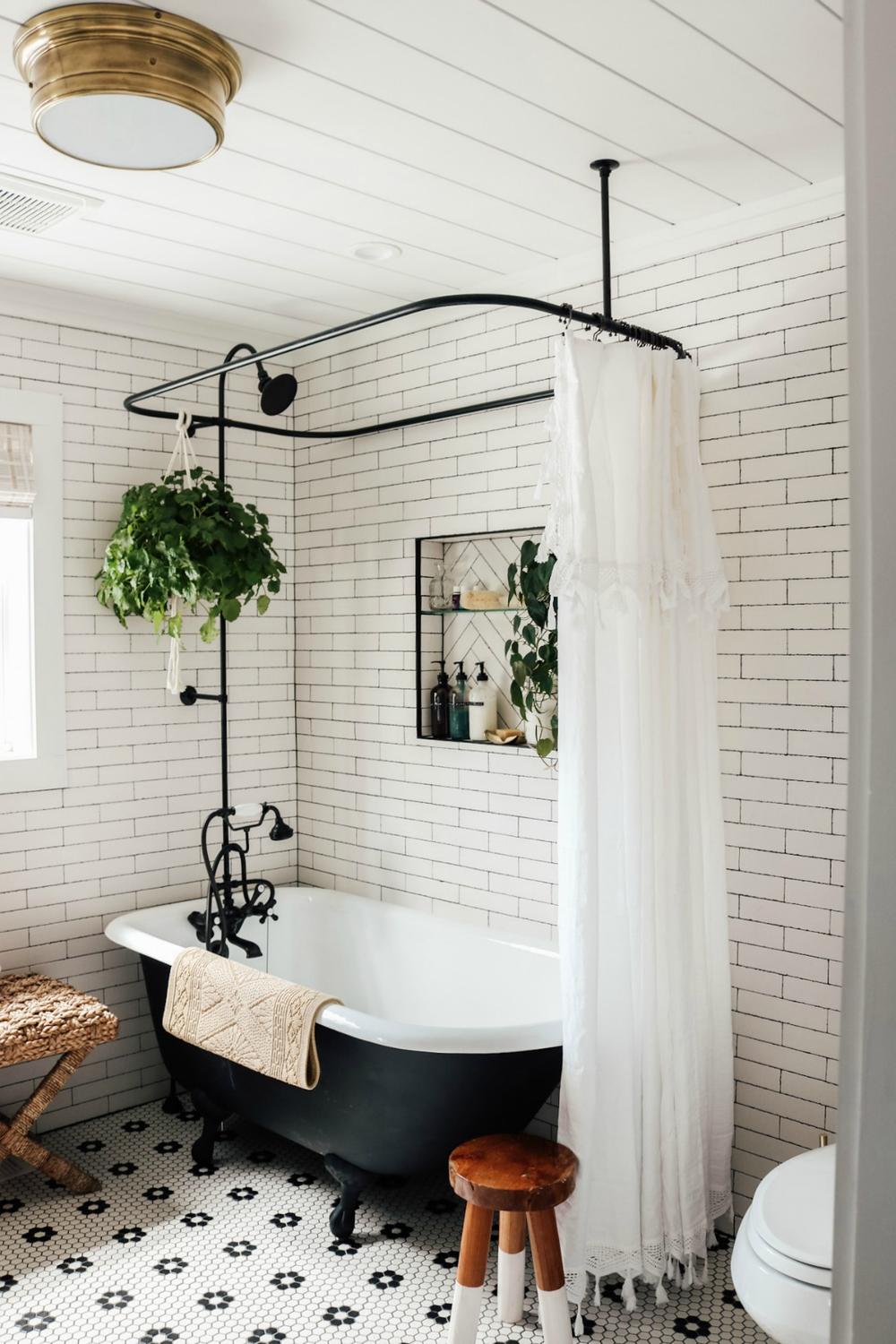 Vintage styled bathroom showcasing a white clawfoot tub with lace detailed shower curtain and mosaic patterned tiles.