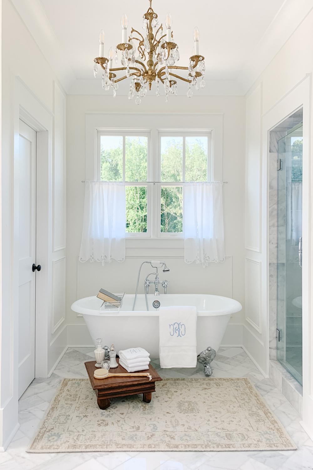 Stylish bathroom featuring a centrally positioned oval clawfoot tub and a chandelier overhead.