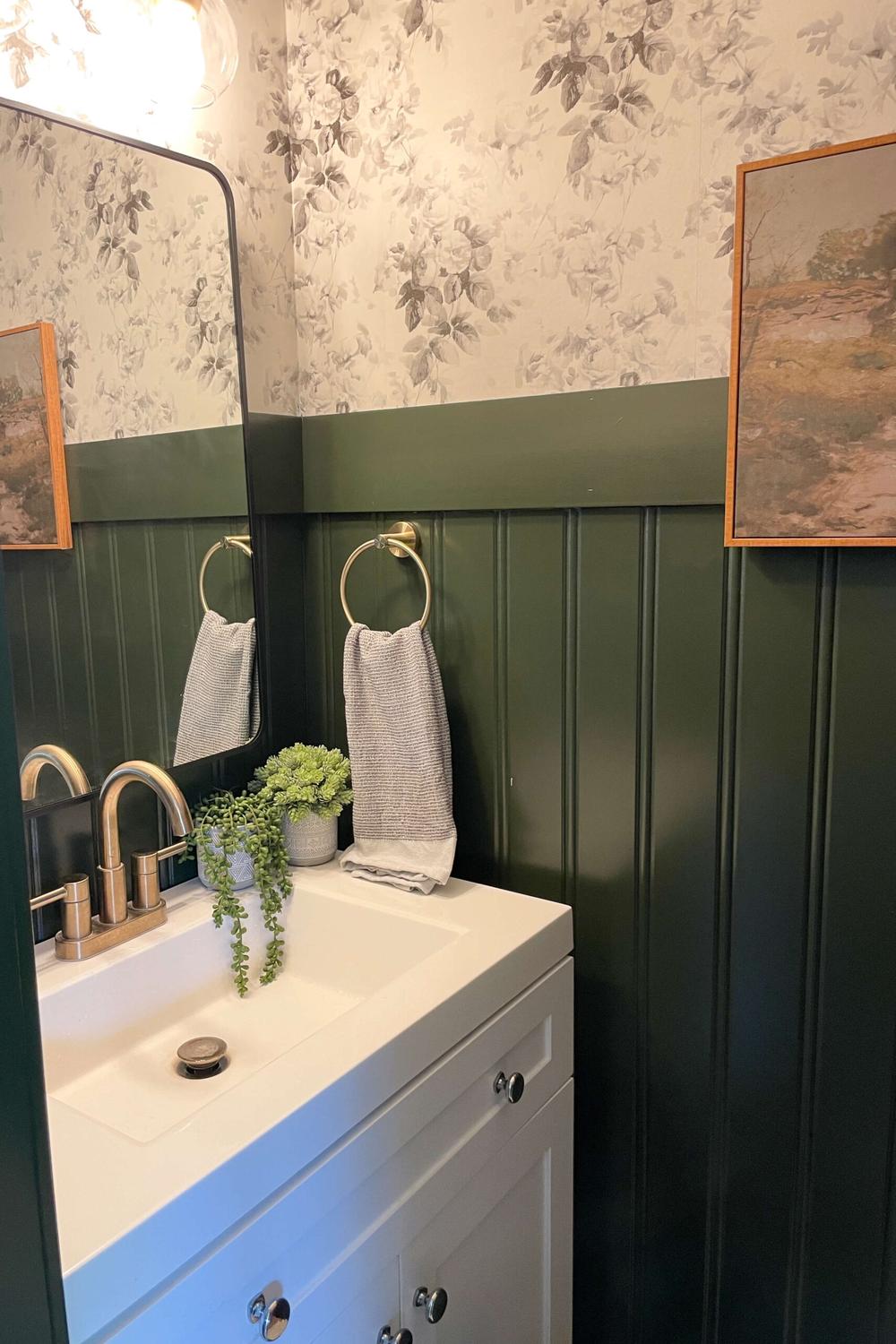 Elegant bathroom featuring deep green beadboard, modern vanity, and artistic decor