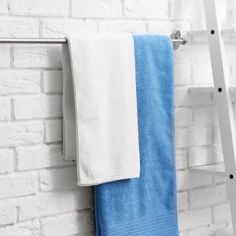 Sleek silver cylindrical towel rack holding white and blue towels against a textured brick wall