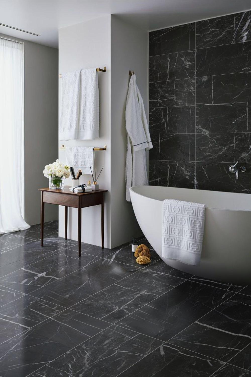 Baño con azulejos de mármol negro y bañera independiente