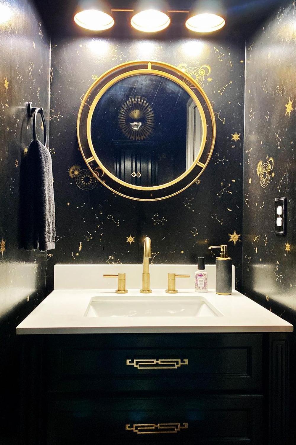A modern bathroom design featuring black cabinetry, gold accents, and celestial motifs.