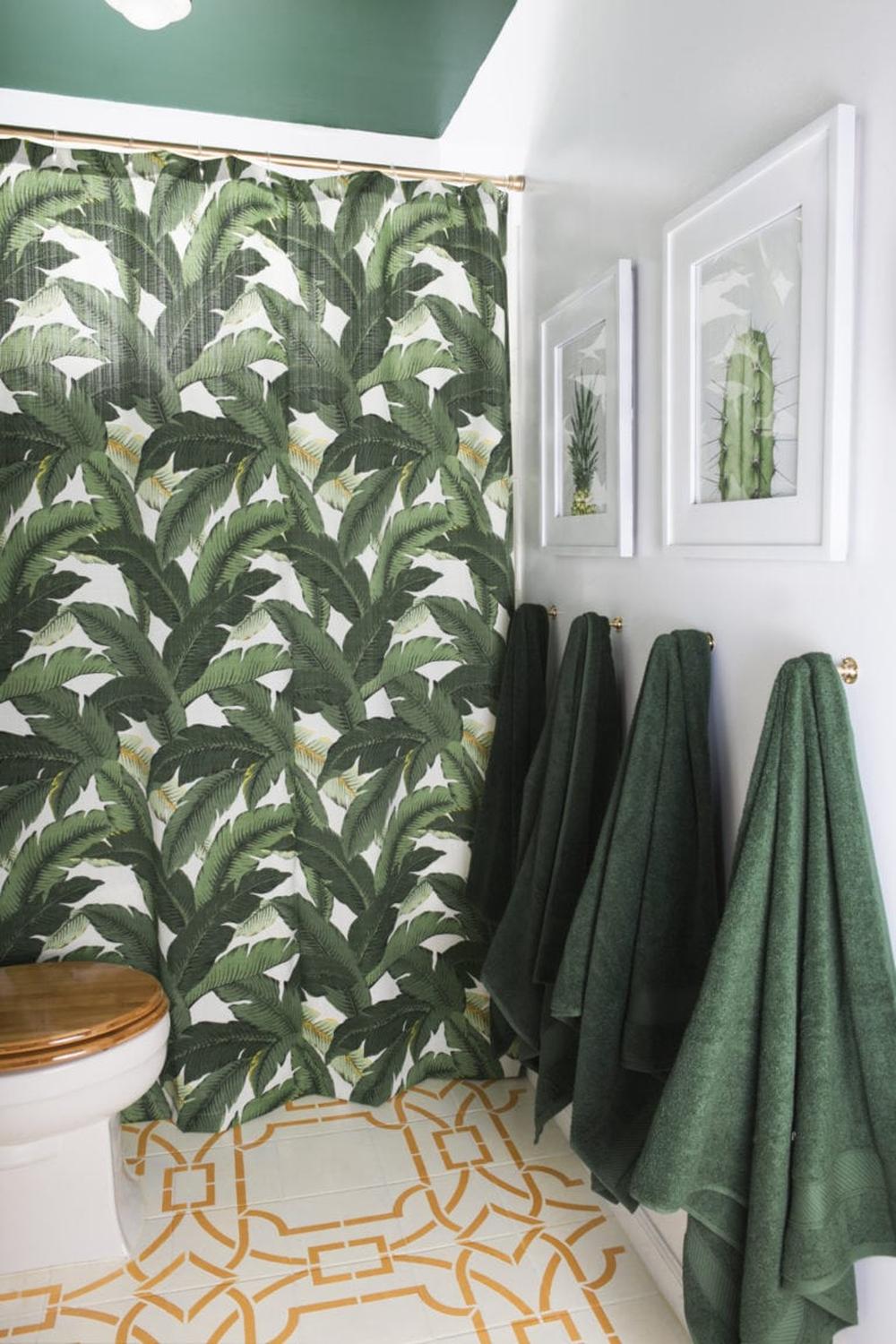 A boho chic bathroom featuring a bold tropical shower curtain and rich green ceiling.