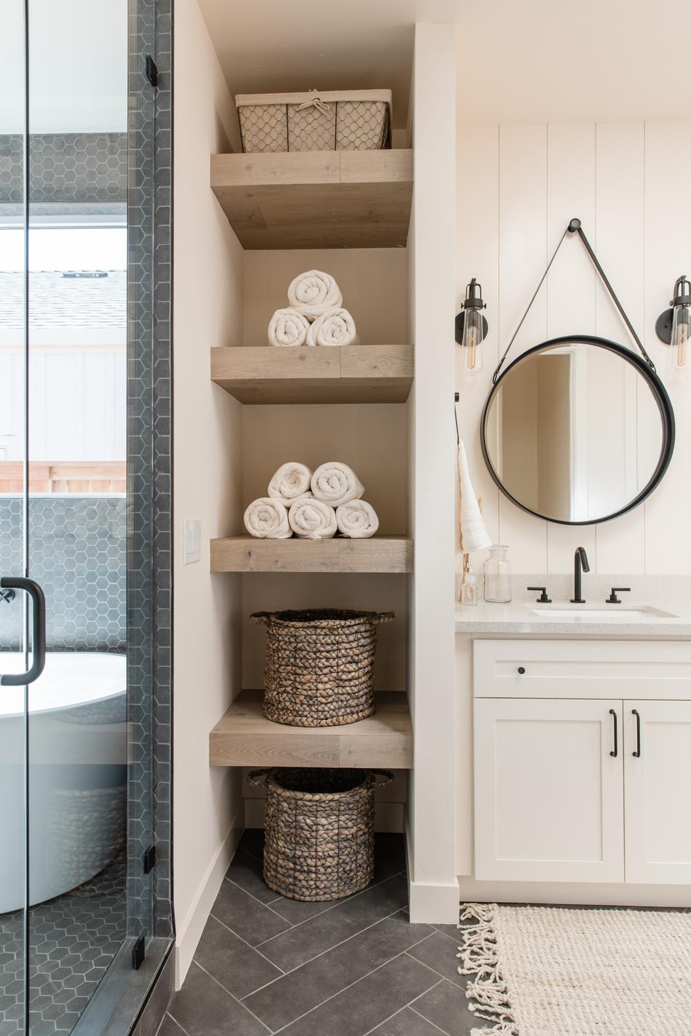 A cozy bathroom featuring light wood shelves with decorative storage baskets and rolled towels for organization.