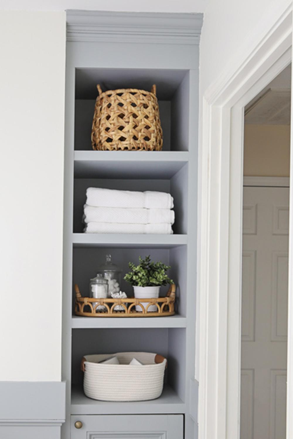 A serene bathroom with light gray shelves artfully organized with decorative elements and storage baskets.