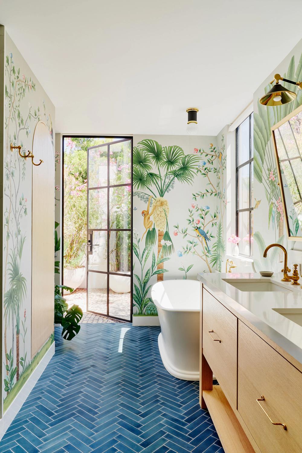 Botanical bathroom featuring blue herringbone cement tiles with natural wooden vanity and freestanding bathtub.