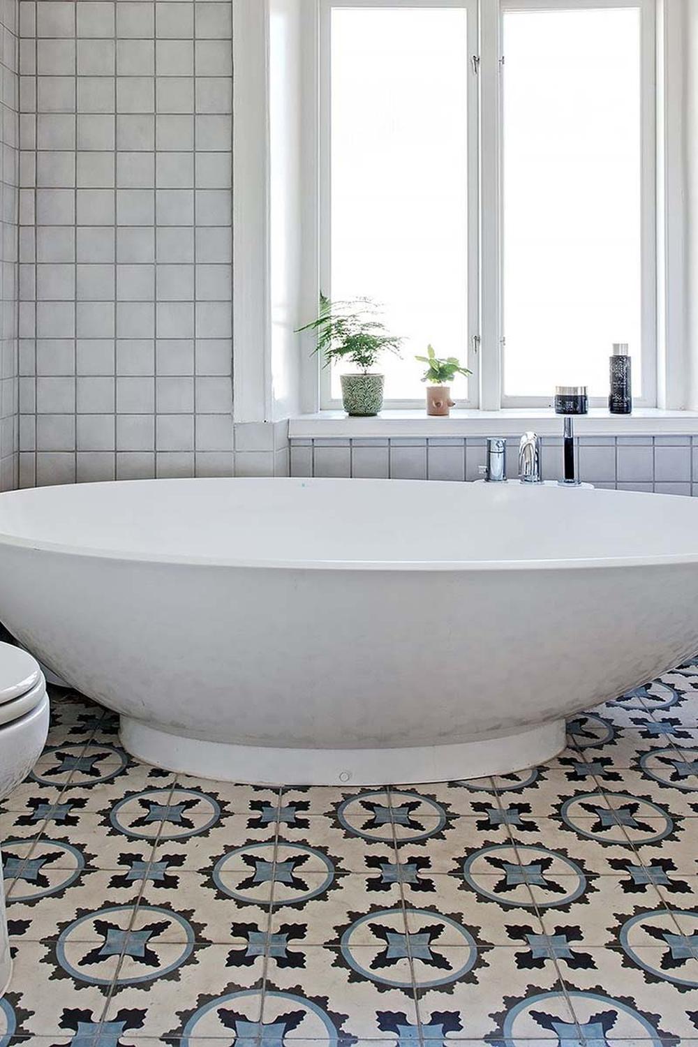 Relaxing bathroom featuring light gray tiles, modern bathtub and decorative window plants.