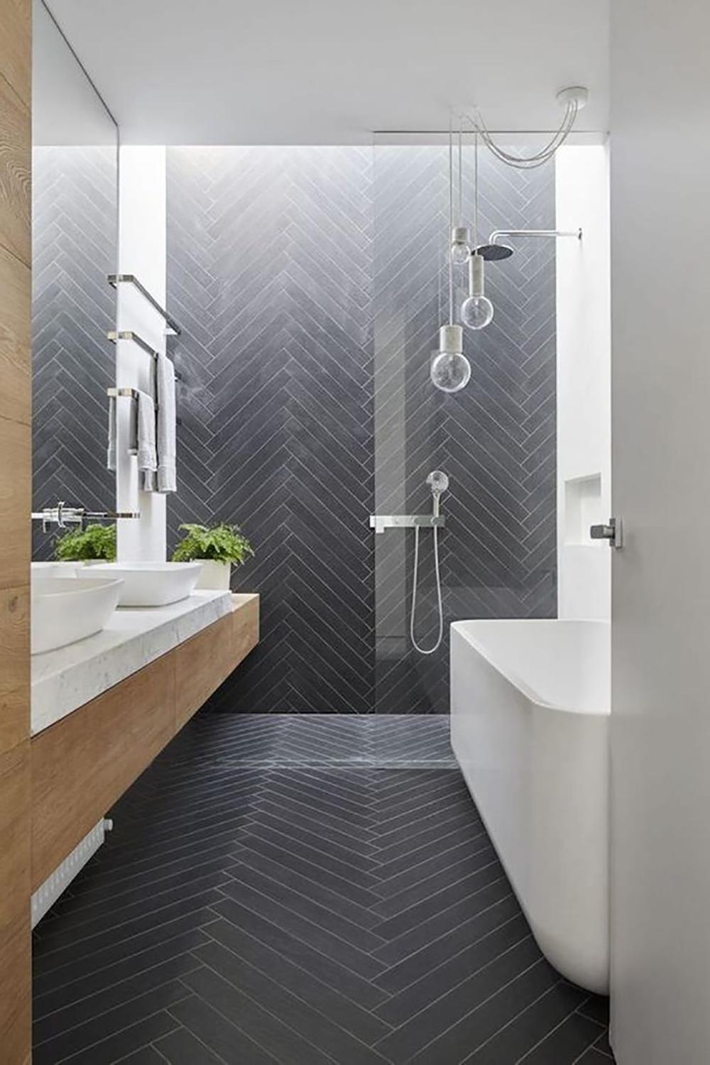 Baño moderno con azulejos en chevron oscuros y elegante mueble de madera.