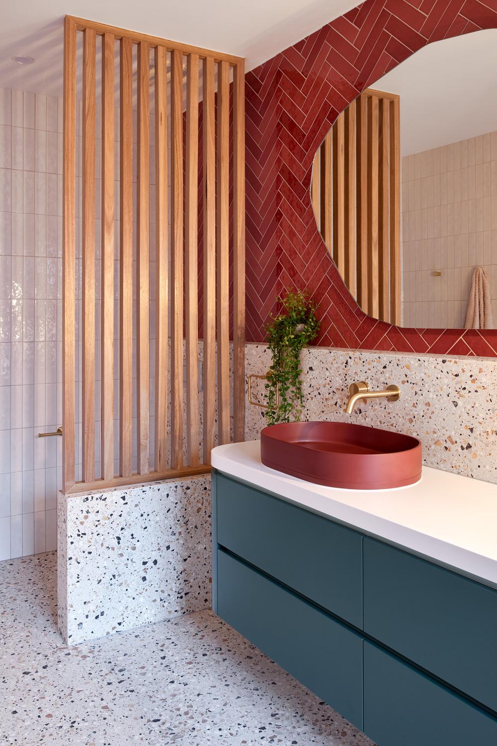 Bold red herringbone tiles in a modern bathroom with deep green cabinetry and a rustic sink.