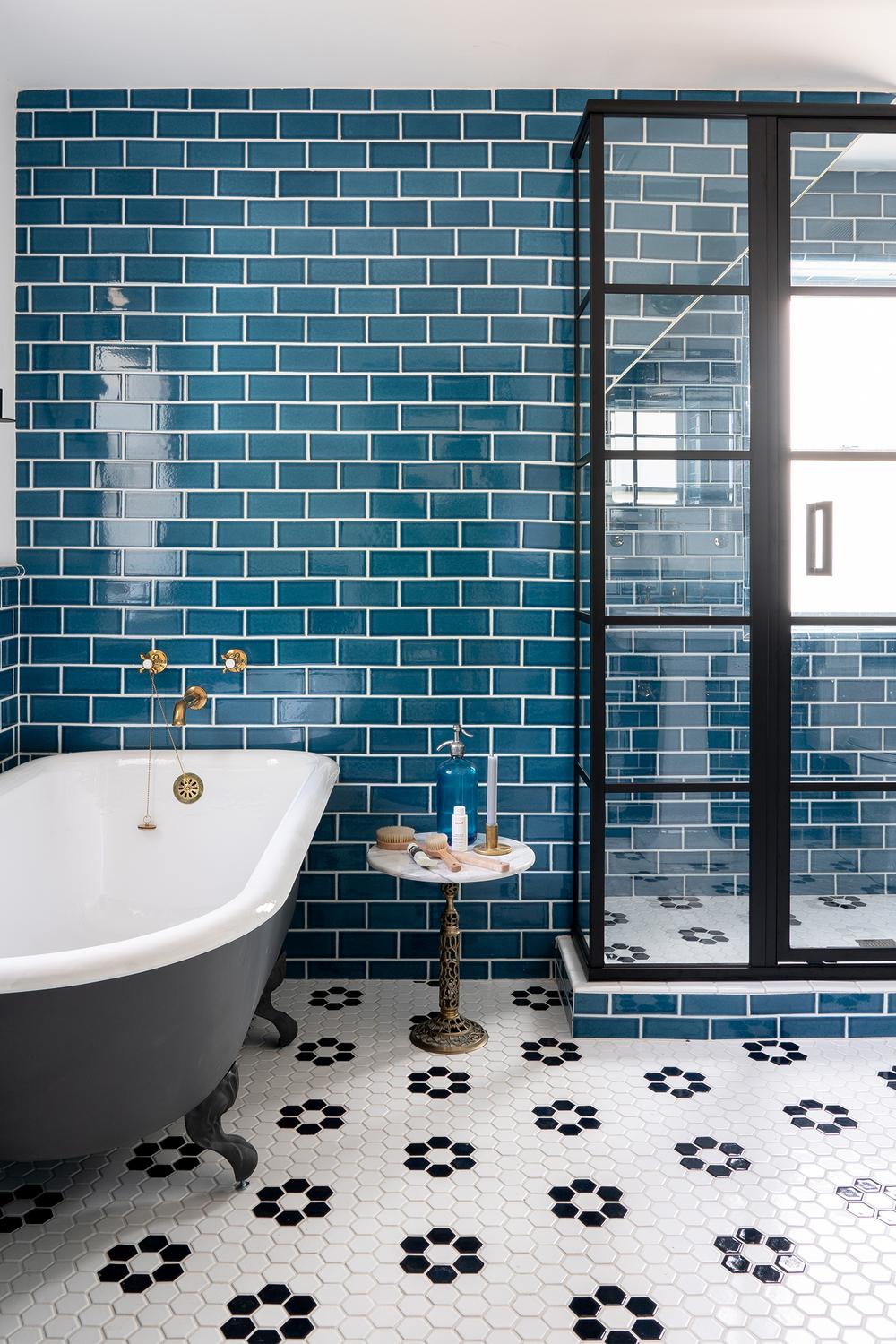 Vibrant teal subway tiles contrasted with black floral patterned flooring and elegant fixtures.
