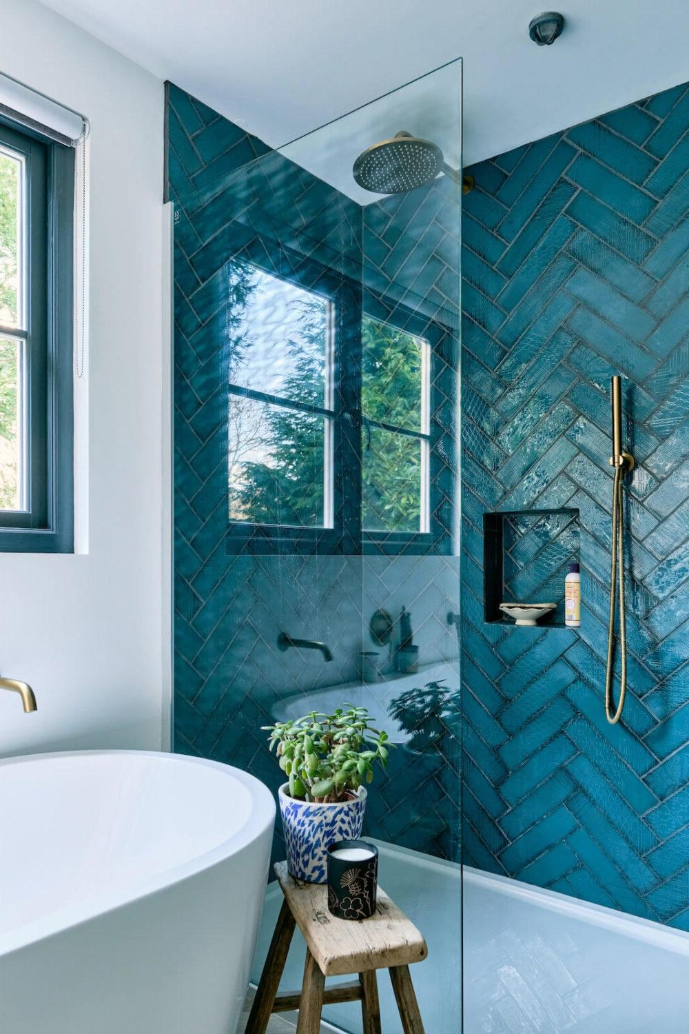 Modern bathroom with striking blue herringbone shower tiles and a sleek gold showerhead.