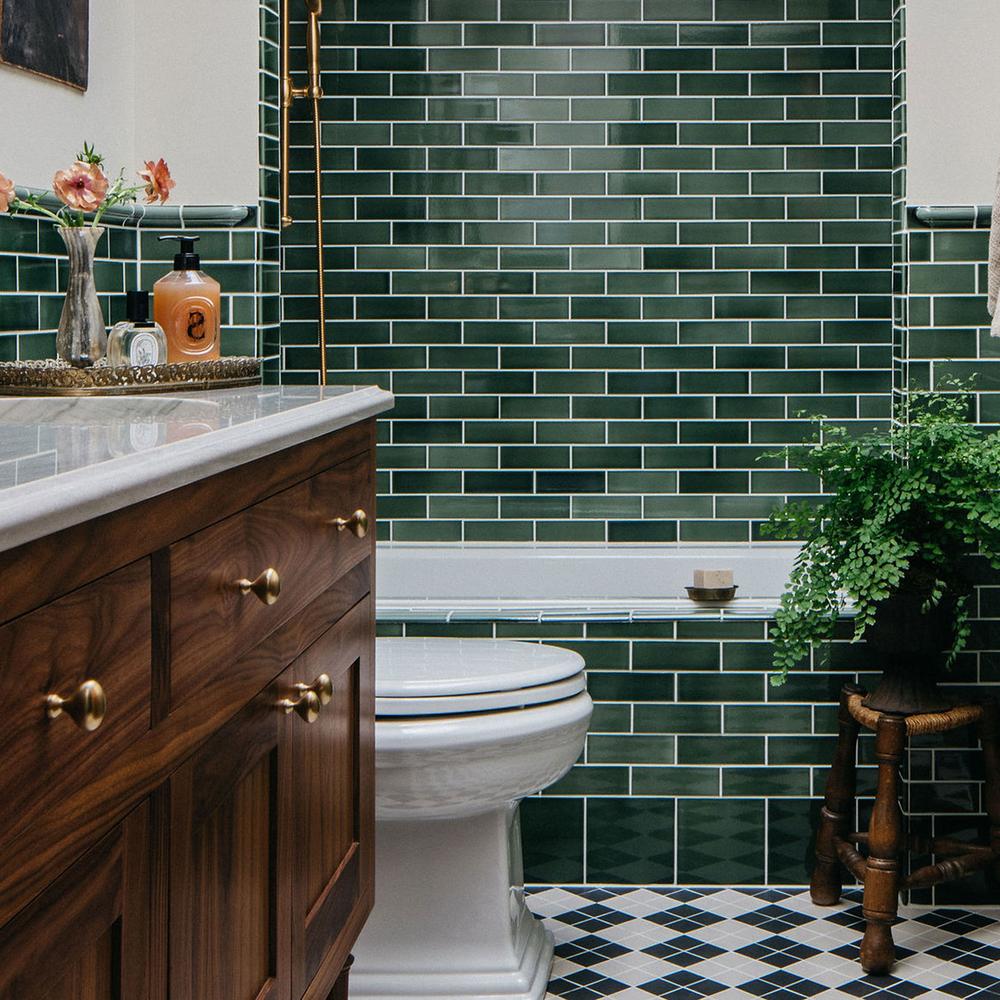 Elegant dark green bathroom showcasing glossy subway tiles and a modern bathtub