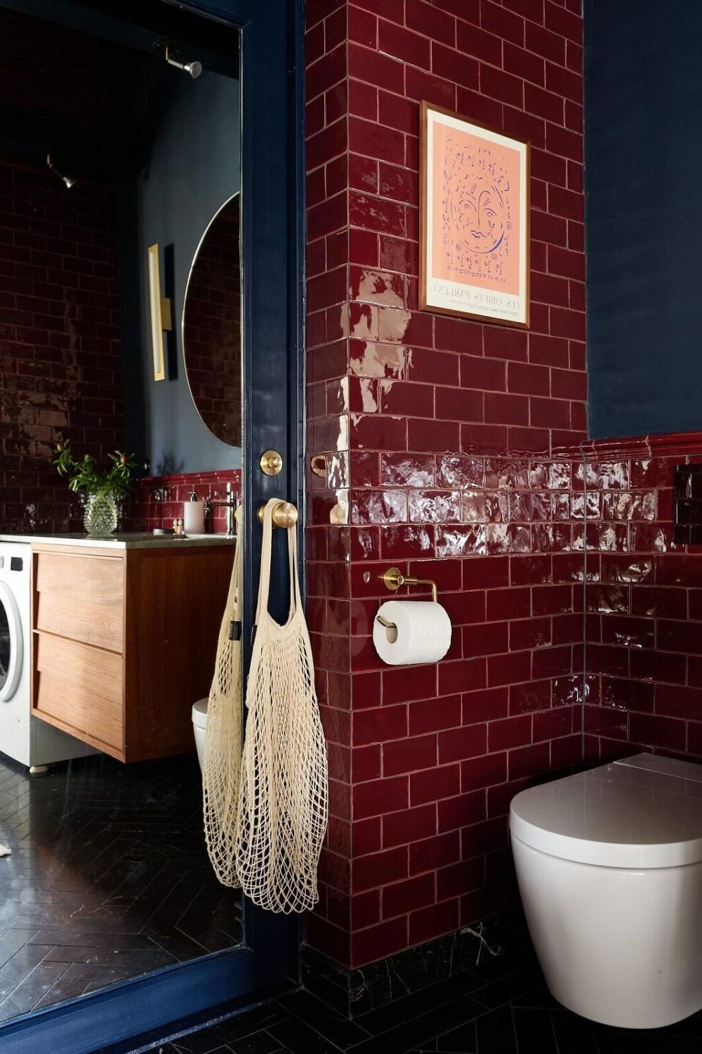 A stylish bathroom featuring glossy dark red subway tiles and navy accents.
