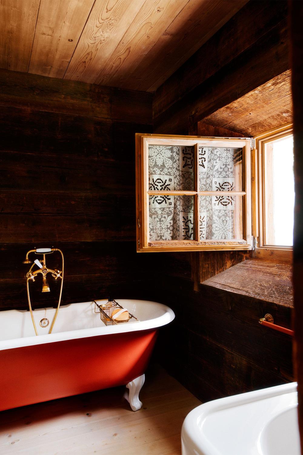 A rustic bathroom showcasing a vintage dark red freestanding bathtub.
