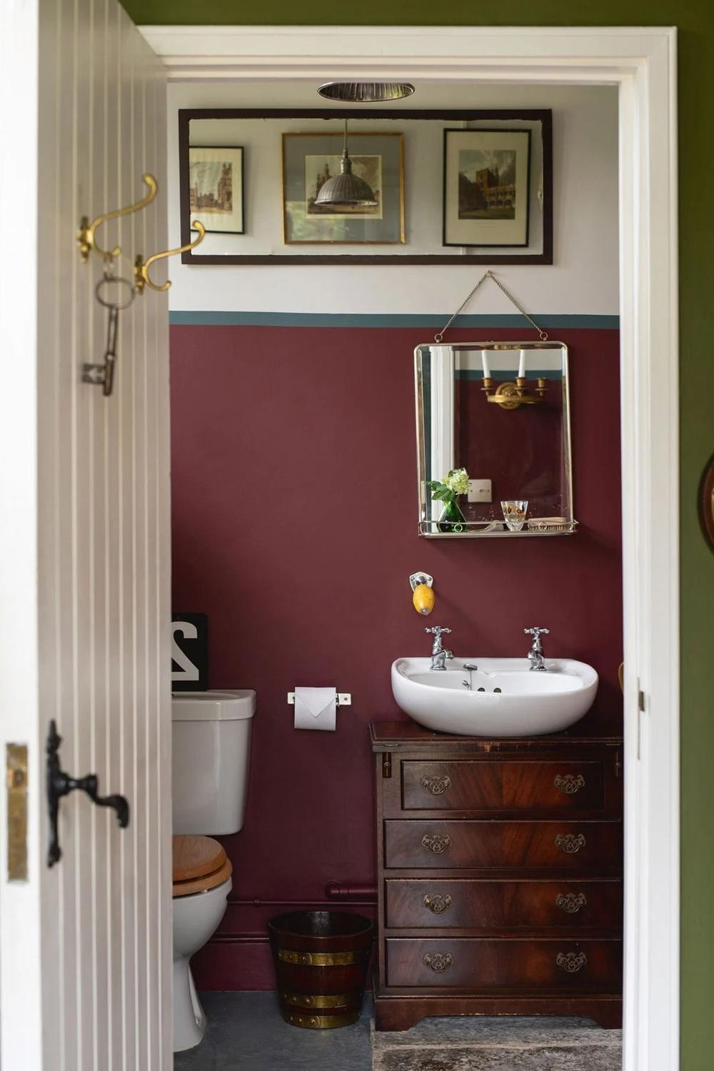 A small dark red bathroom featuring expressive decor and vintage elements.