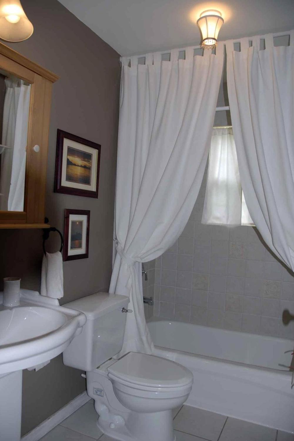 Timeless bathroom design with white double shower curtains against a warm gray wall and a stylish ceiling light.