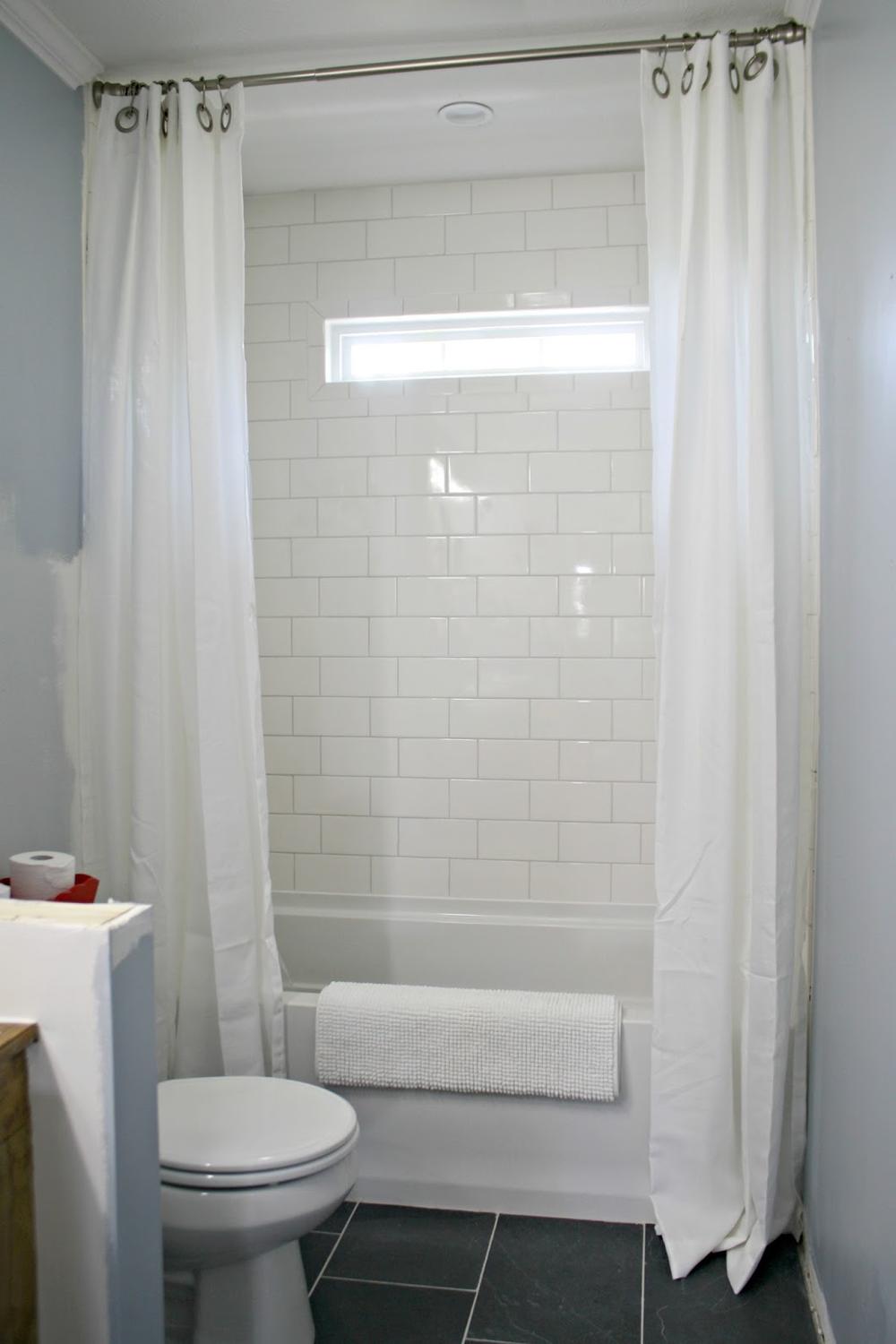 Stylish bathroom featuring white sheer double curtains over a soothing light blue wall.