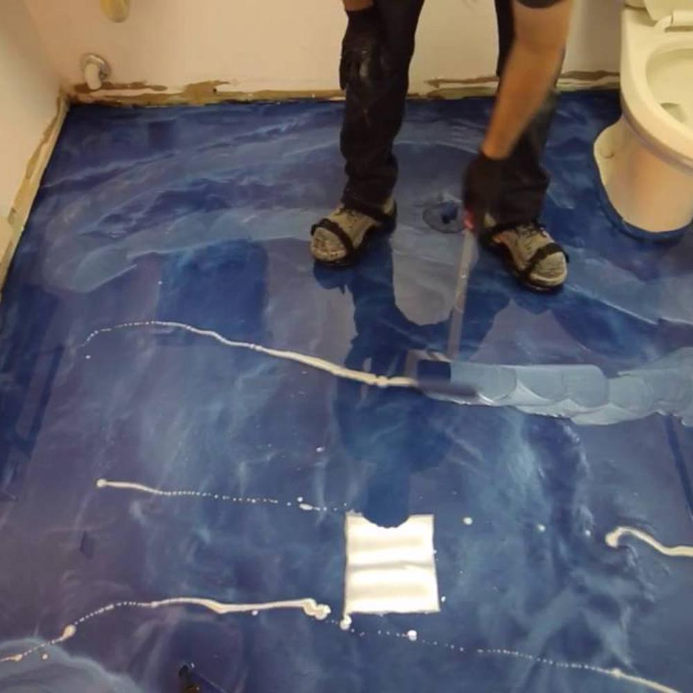 Bathroom floor being coated with blue epoxy, showcasing the transformation process.