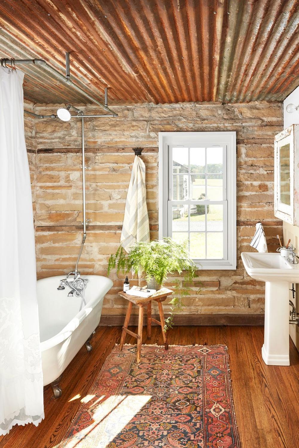 Farmhouse bathroom with rustic decor featuring corrugated metal ceilings, clawfoot tub, and warm wood accents.