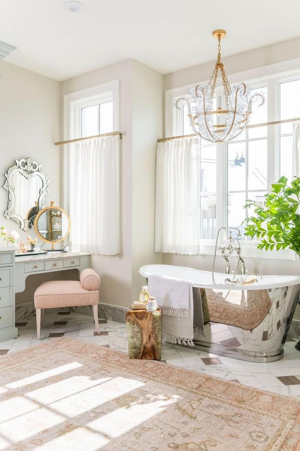 A beautifully designed feminine bathroom featuring a light blue vanity, a freestanding bathtub, and elegant chandelier lighting.