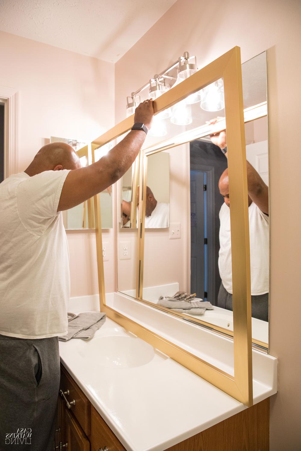 A man aligns a stylish mirror frame with industrial lighting in a streamlined bathroom.