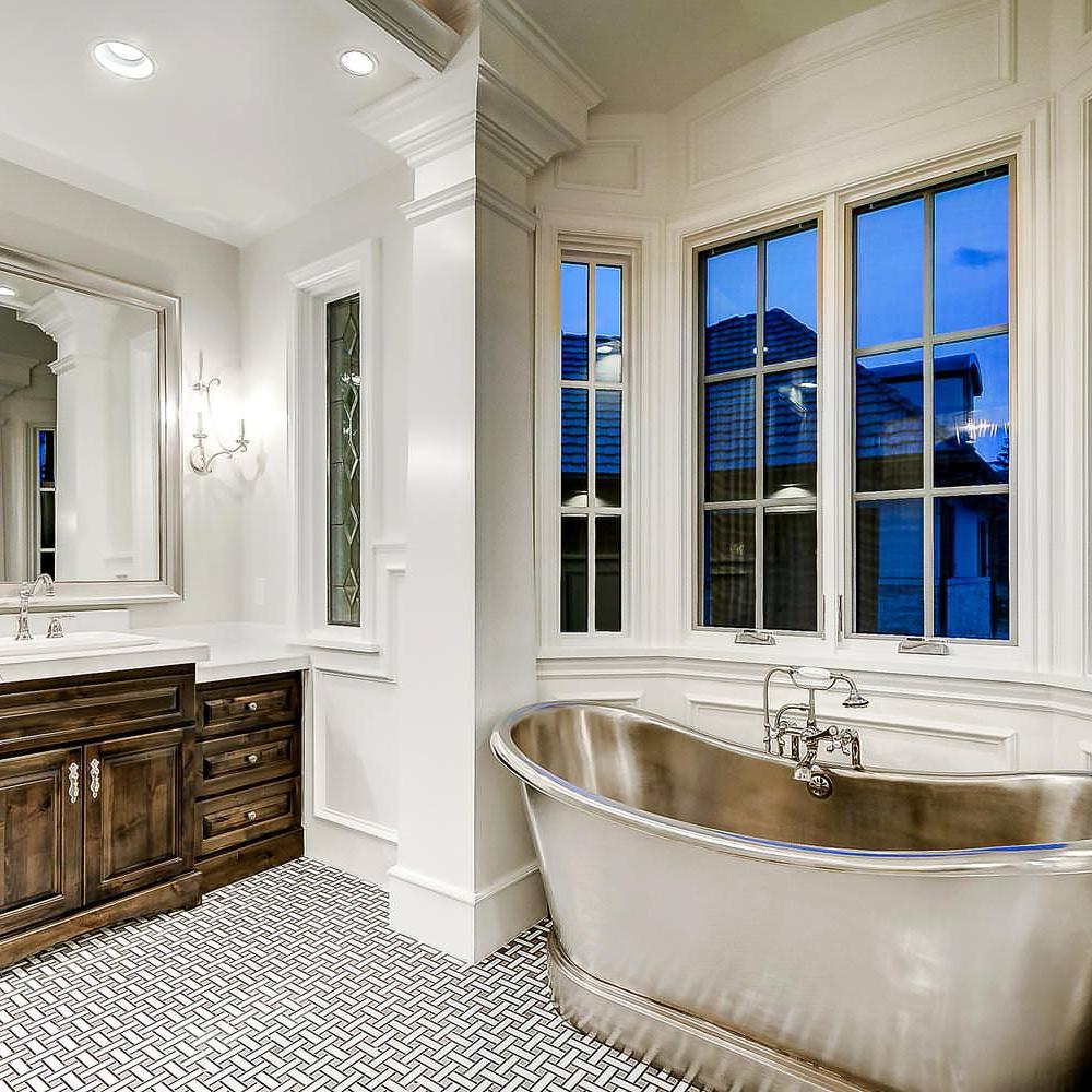 A bright French country bathroom featuring a polished freestanding tub and bay windows.