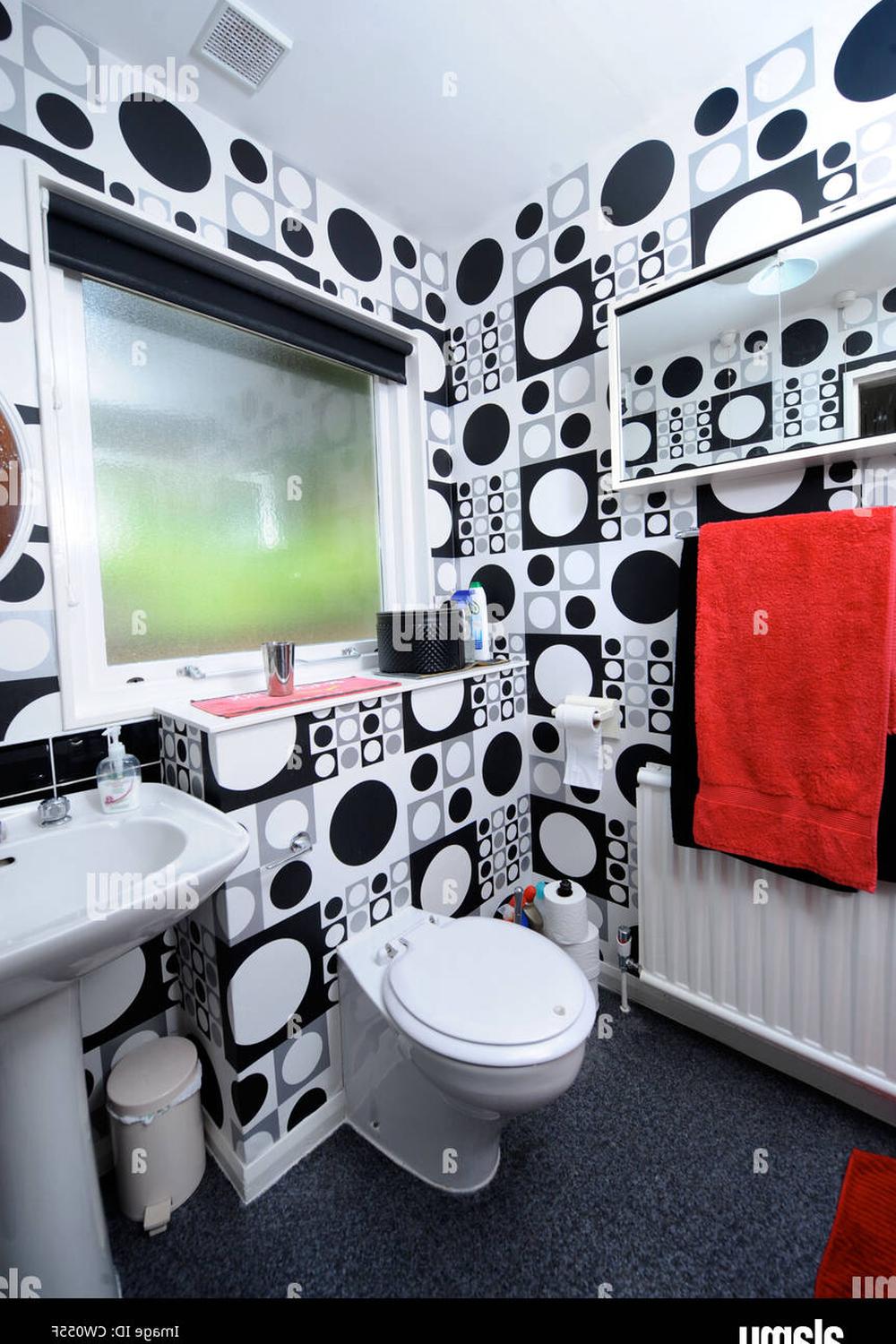 A lively bathroom decorated with bold black and white polka dot wallpaper, featuring a sleek white sink and vibrant red towel.