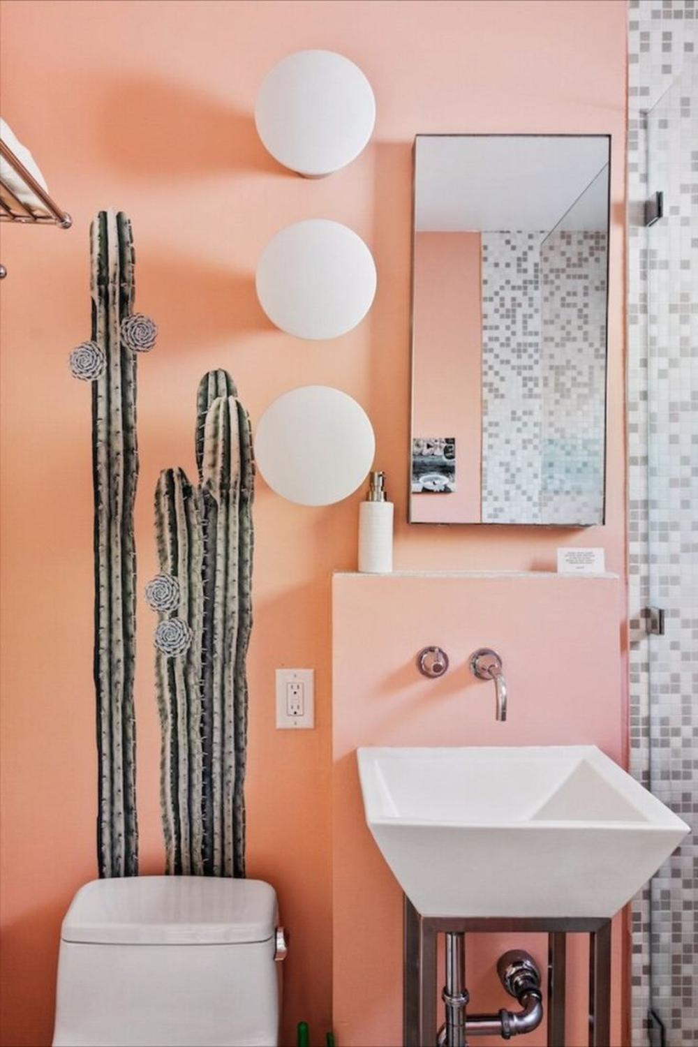A bathroom featuring peach walls with decorative cacti, a striking geometric washbasin, and modern lighting.