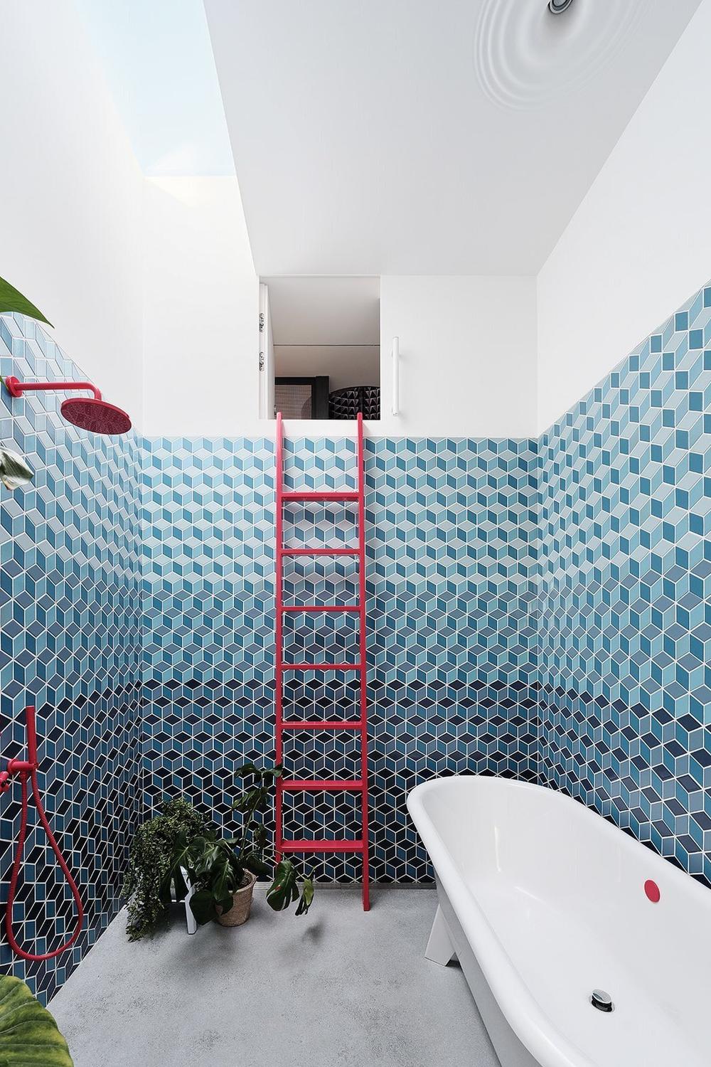 A modern bathroom showcasing blue hexagonal mosaic tiles, freestanding bathtub, and a vibrant red ladder.