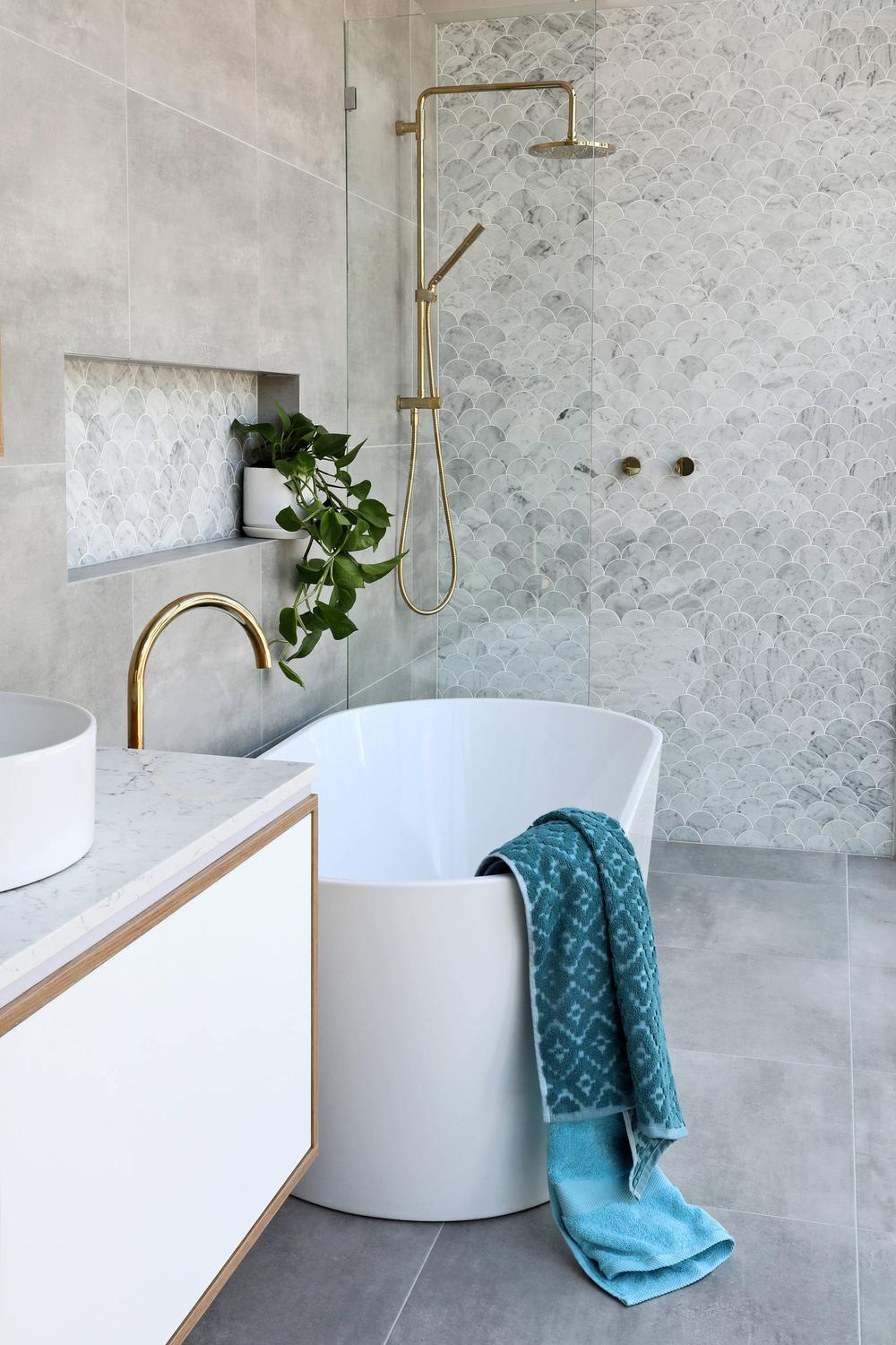 Baño moderno en blanco con bañera independiente y acabados metálicos dorados