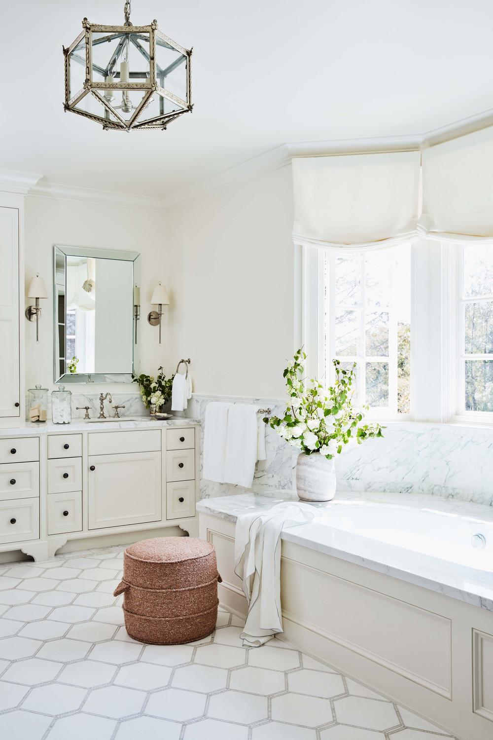 An elegant white bathroom with beautiful natural light, stylish decor, and a freestanding tub.