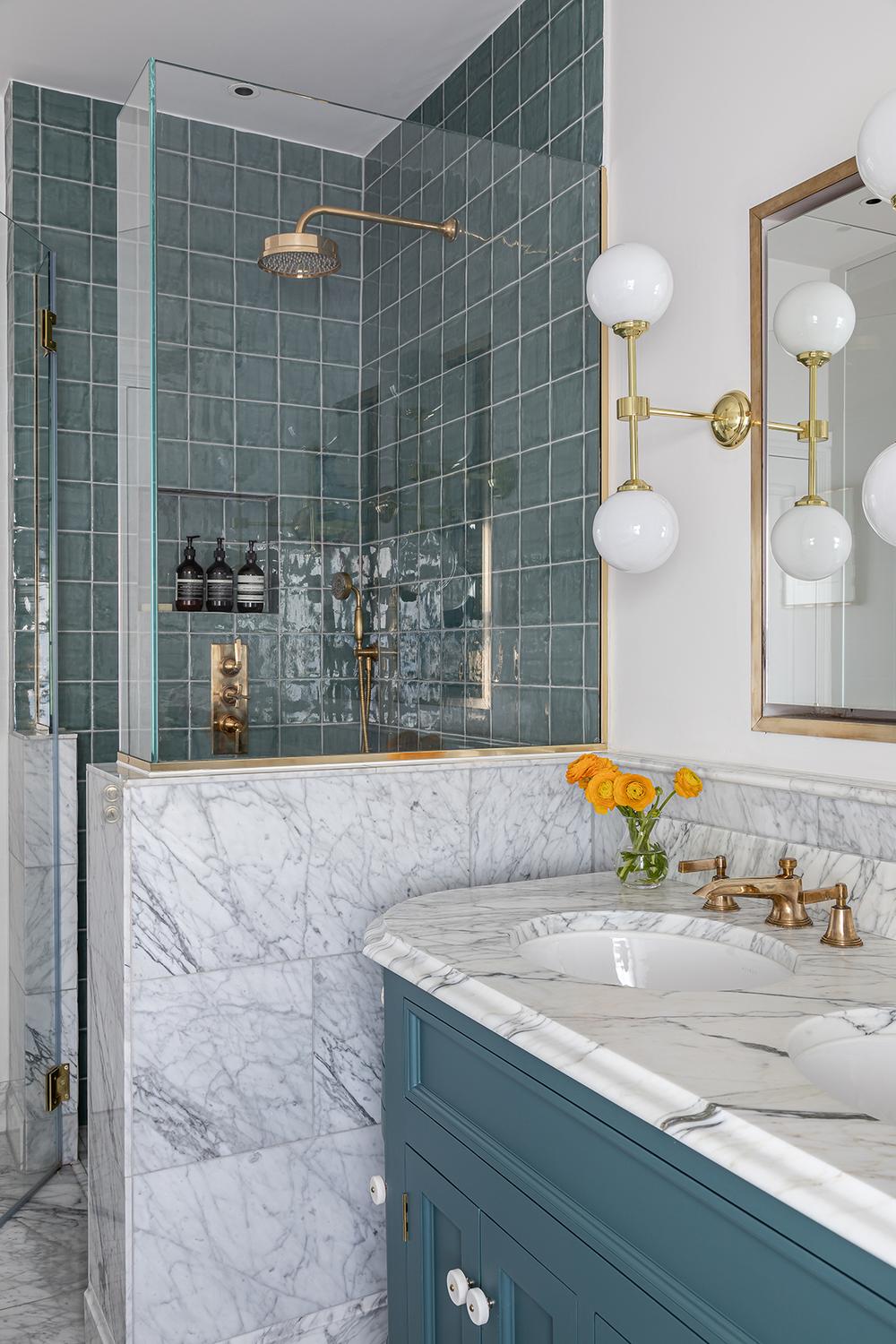 An eclectic bathroom featuring sea-green tiles and a deep blue vanity, accented with luxurious gold faucets and fixtures.